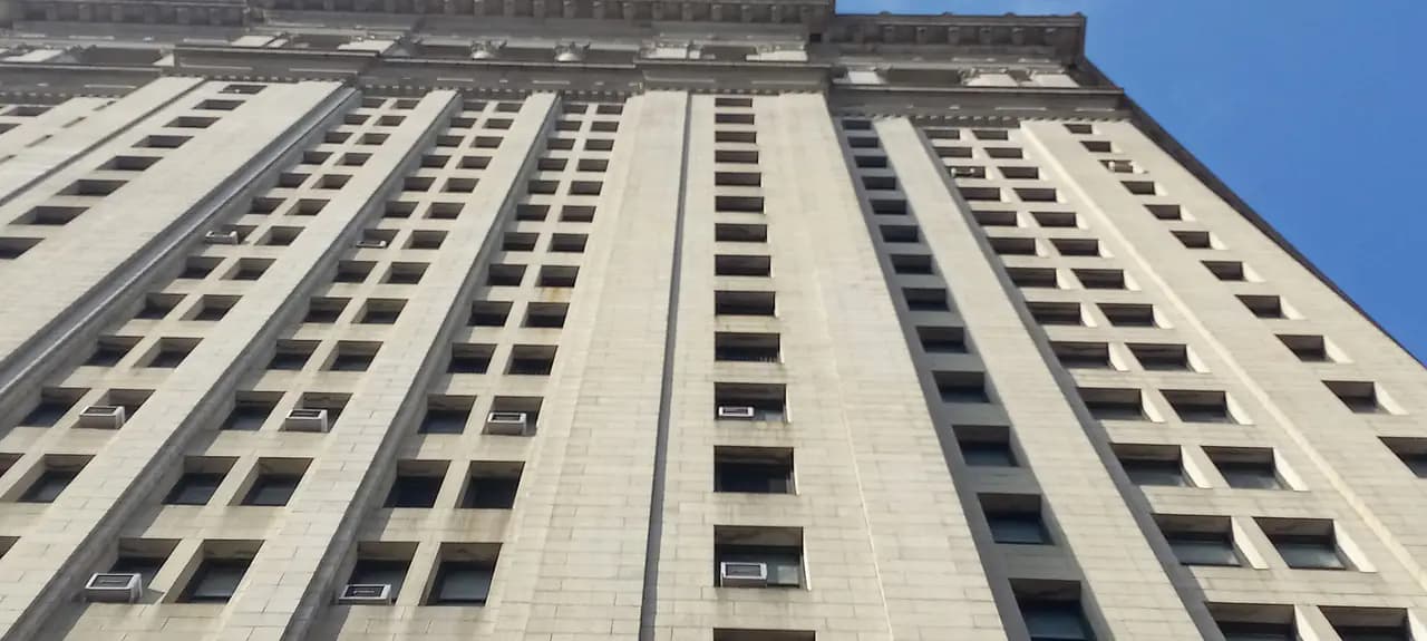 Looking up at the gray stone facade of the Manhattan Municipal Building against a blue sky