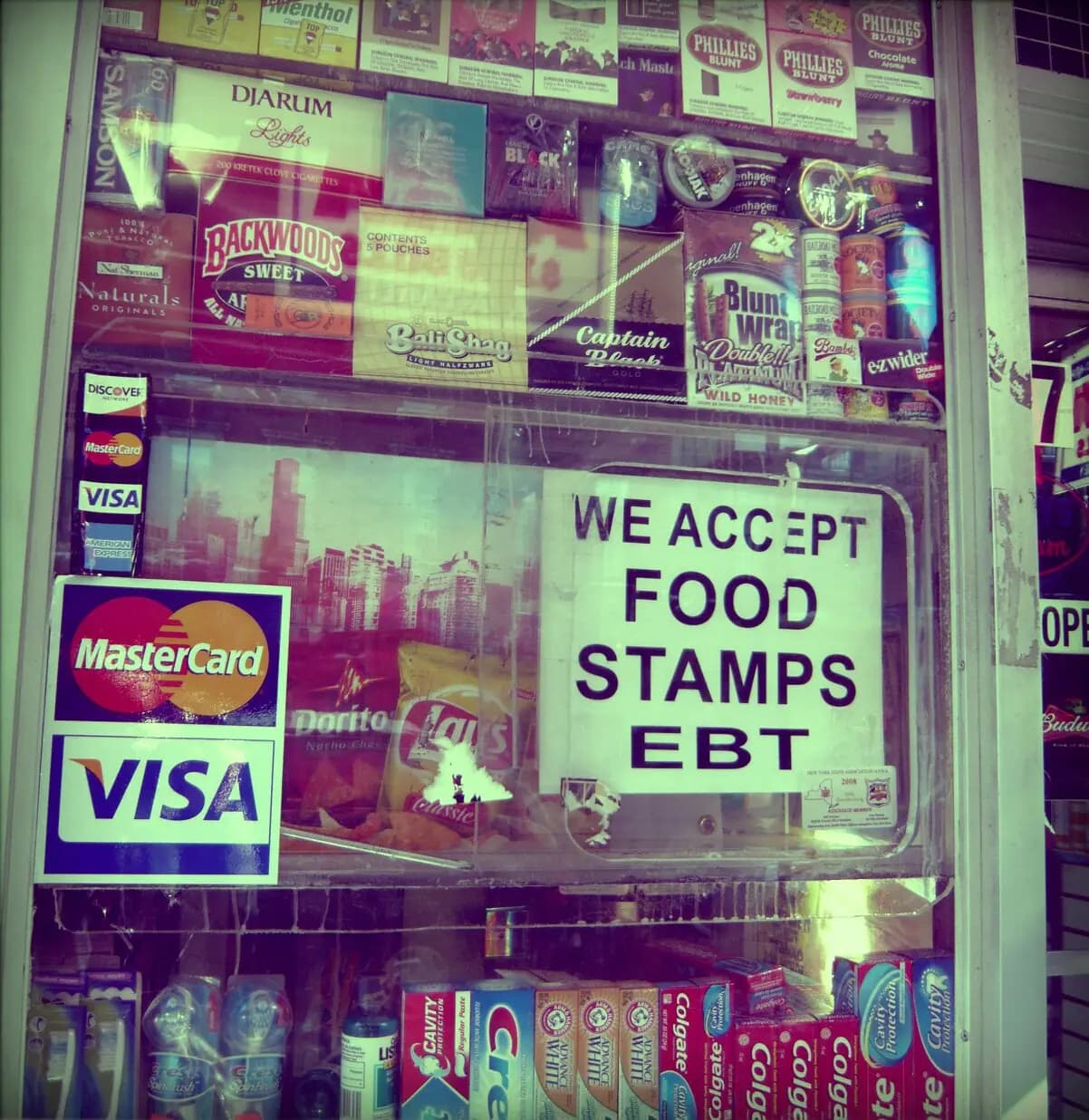 A Brooklyn deli window with a sign reading 'We accept food stamps EBT' next to credit card decals