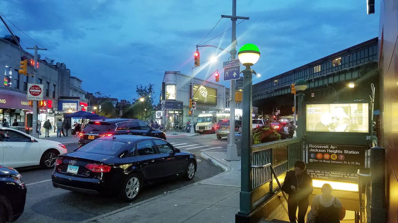 Restaurants and shops at dusk at Roosevelt Avenue and 74th Street in Jackson Heights, Queens, with the elevated 7 train and a subway entrance