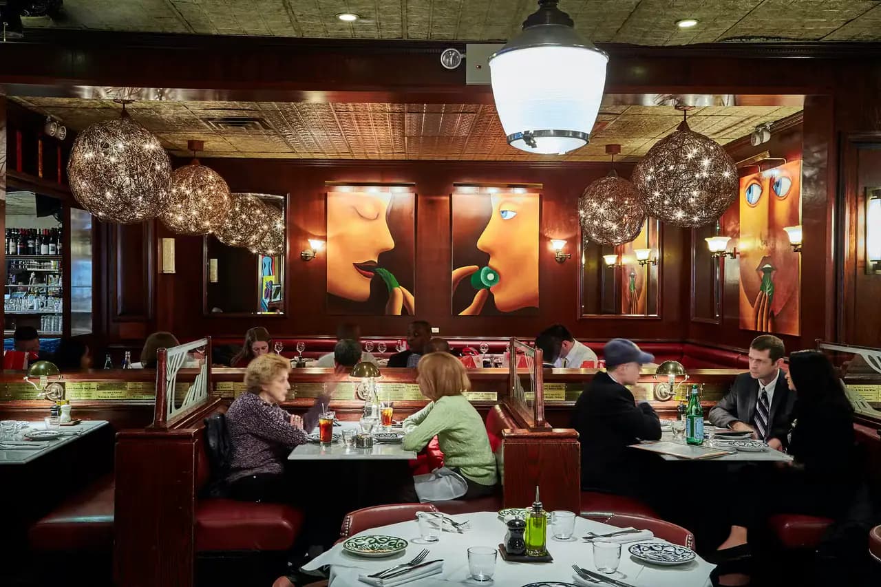 The wood-paneled dining room of Café Fiorello, with red banquettes, white tablecloths and a chef tending the antipasto bar in the foreground