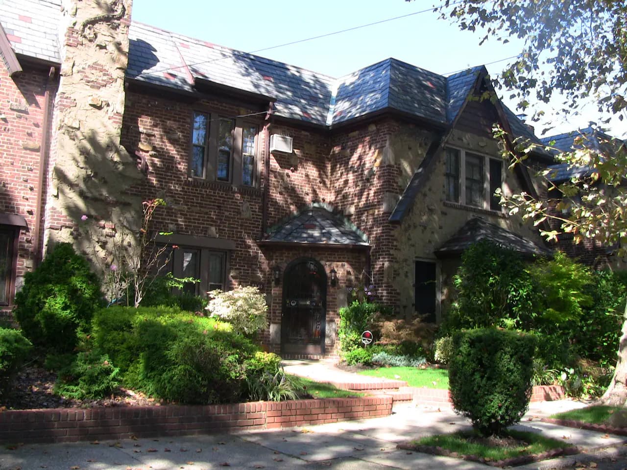 Brick and stucco attached Tudor-style houses with slate roofs and front gardens on a residential street in North Flushing