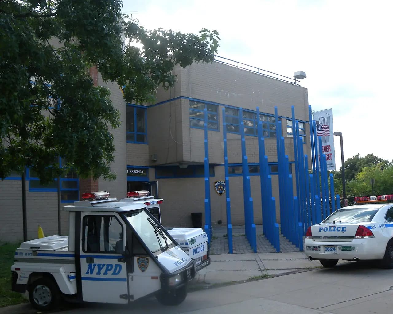 The NYPD 49th Precinct stationhouse in the Bronx, a tan building with blue vertical fins, with a police vehicle parked out front