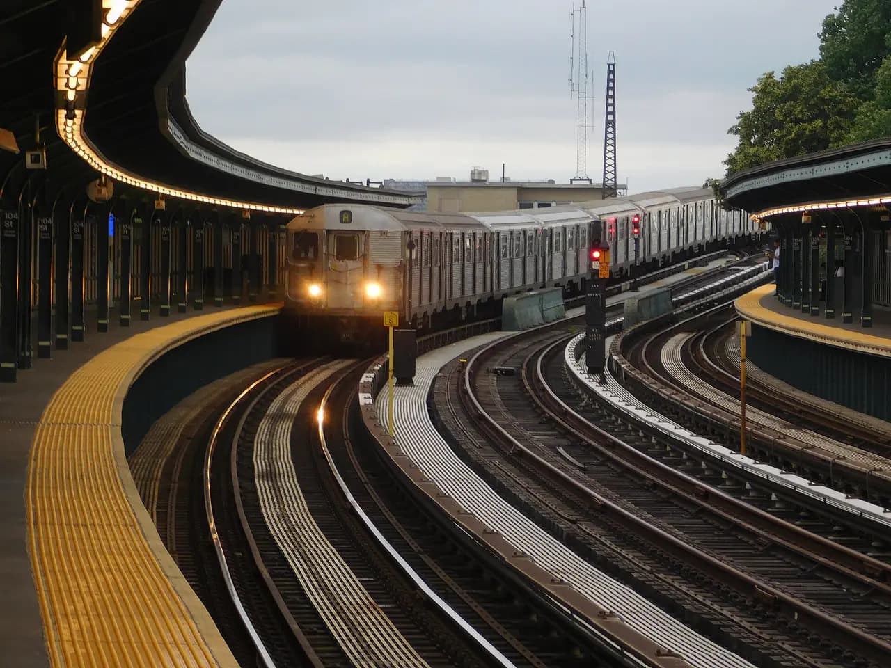 An A train rounds the curve into the elevated 104th Street station on the Fulton Street Line in Ozone Park, Queens, with signals along the tracks