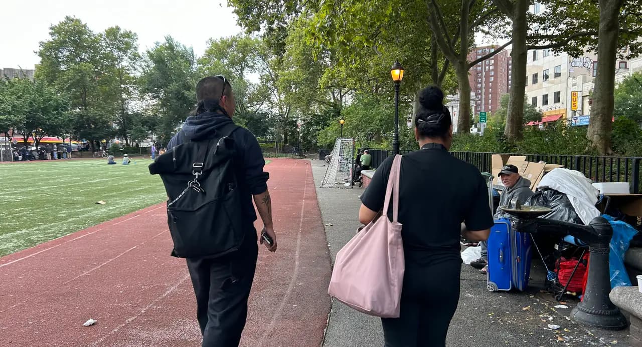 Two outreach workers walk along a park path in Manhattan past a man sitting with his belongings