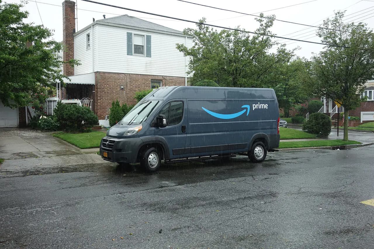 An Amazon Prime delivery van parked on a wet residential street lined with houses in Hillcrest, Queens