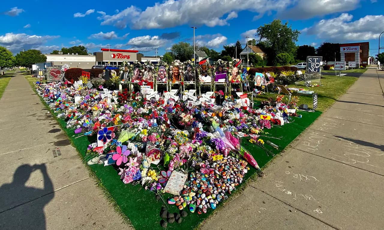Flowers, painted stones and portraits at a sidewalk memorial on Jefferson Avenue, with the Tops supermarket sign behind