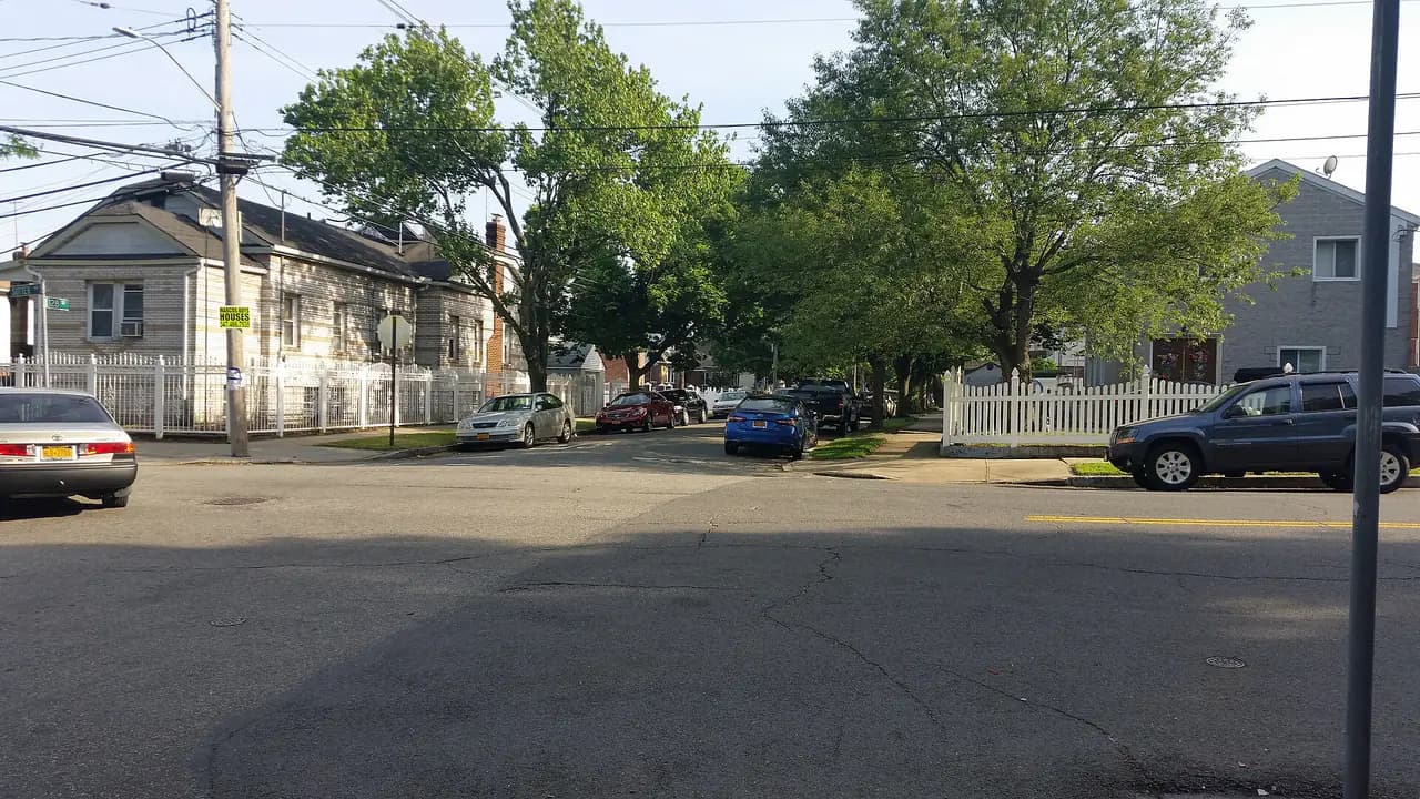 A quiet residential intersection of detached houses and trees in South Ozone Park, Queens