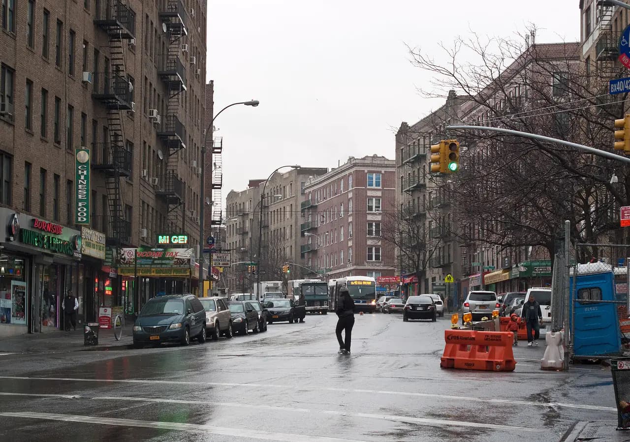 Apartment buildings and storefronts along Burnside Avenue at Loring Place in Morris Heights on a wet winter day