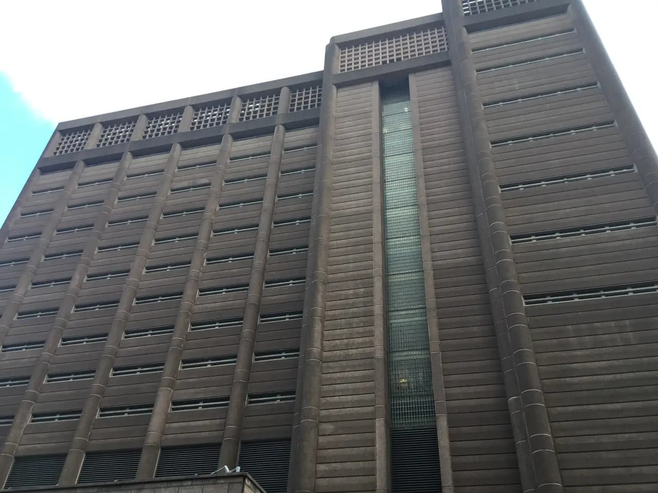 A tall brown concrete jail tower with narrow vertical windows, seen from the street below