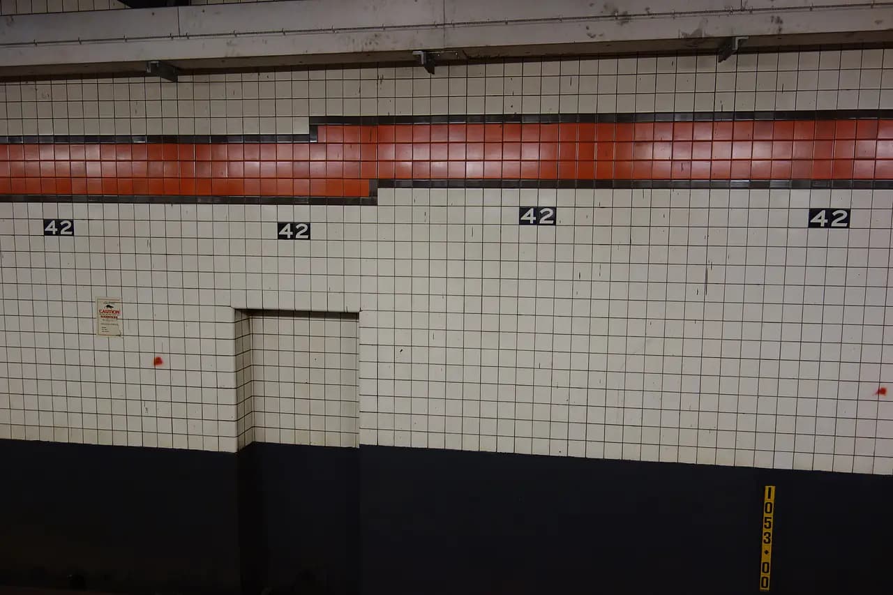 The uptown platform of the 42nd Street-Bryant Park subway station with red columns and overhead signs