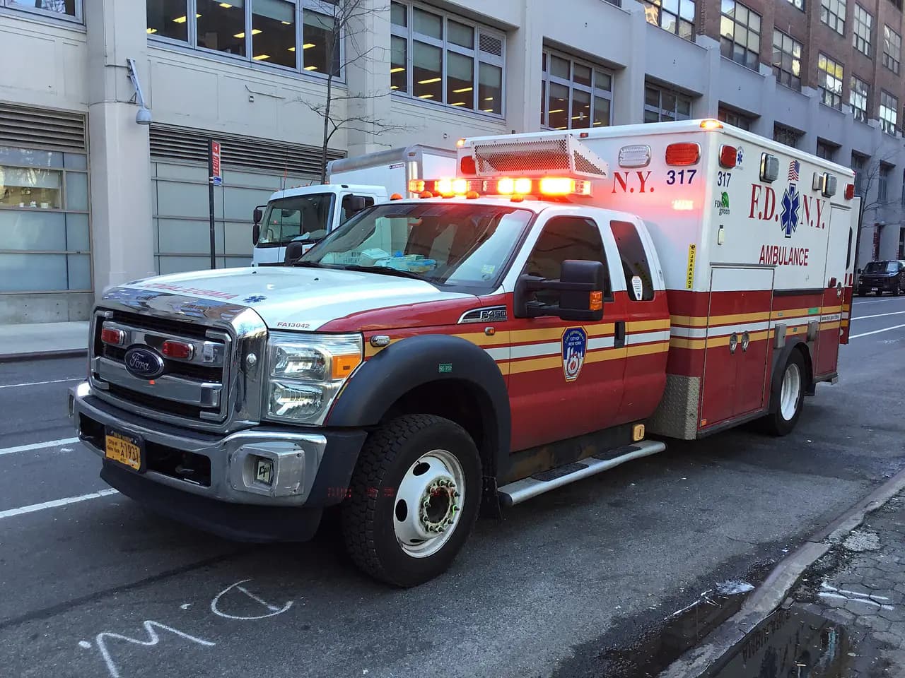 An FDNY ambulance with its emergency lights on parked on a street in Chelsea, Manhattan