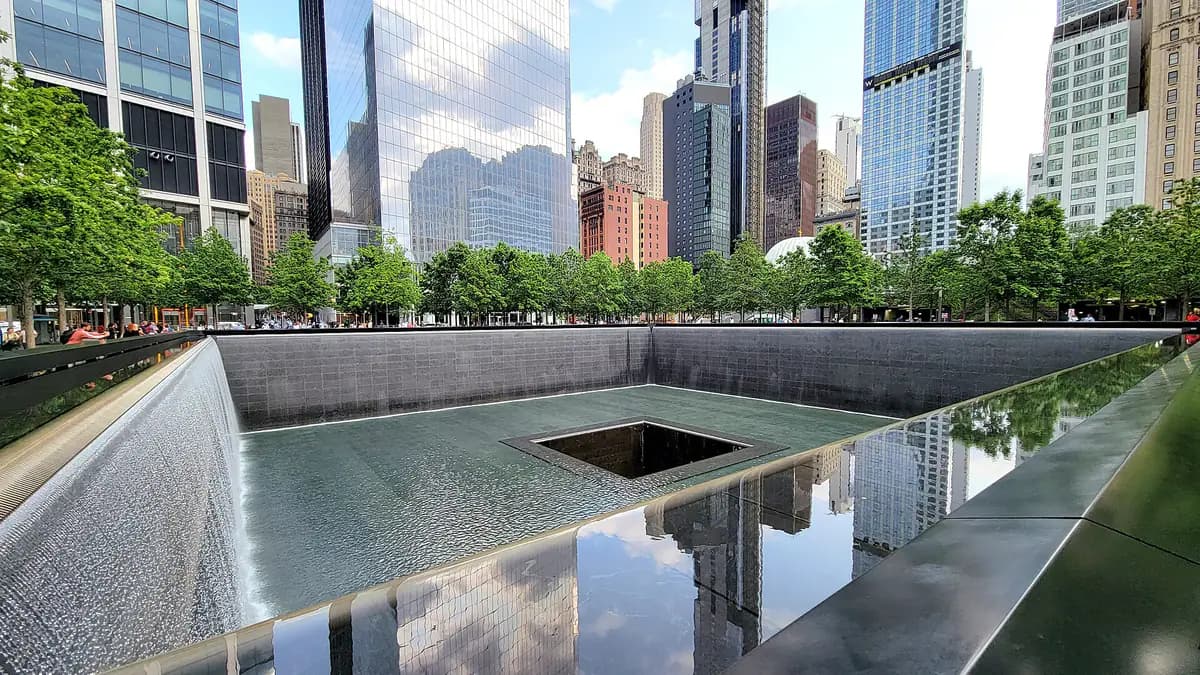 Water falls into the South Pool of the National September 11 Memorial, surrounded by bronze parapets and trees