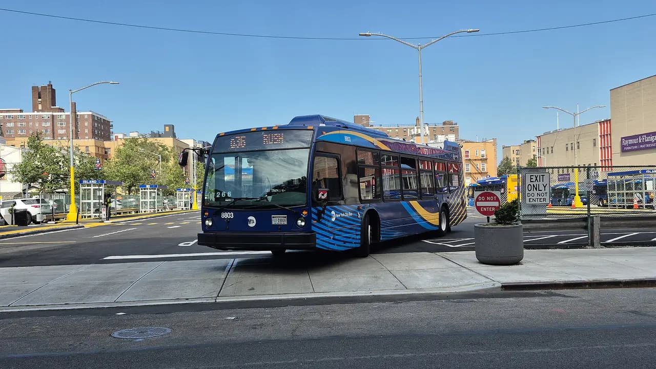 A blue MTA New York City Bus marked 8803 turning out of a bus terminal on a sunny day