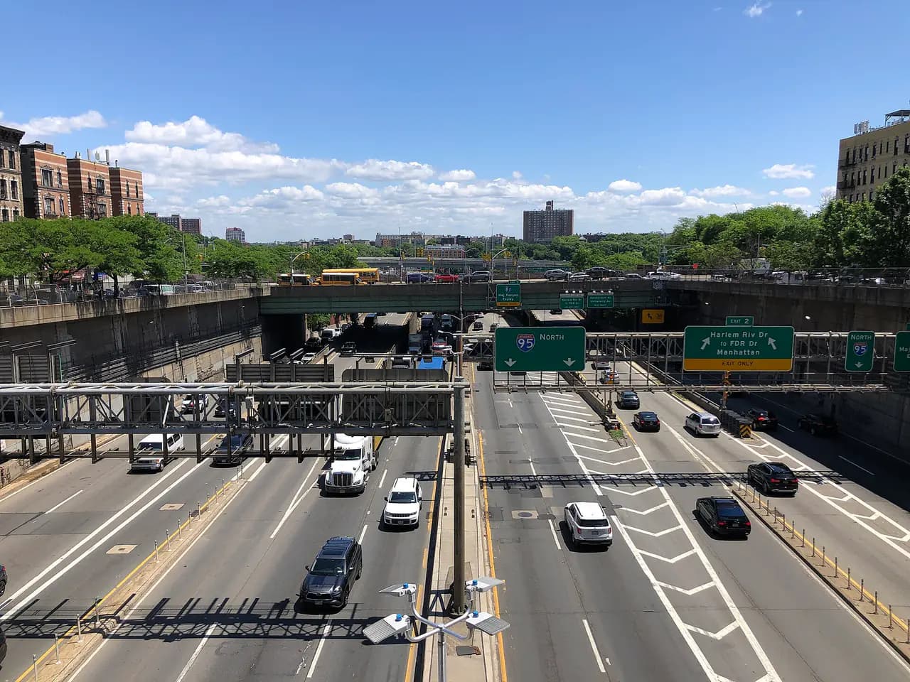 Traffic on the multi-lane Trans-Manhattan Expressway in a sunken trench between apartment buildings in Washington Heights, with I-95 signs overhead