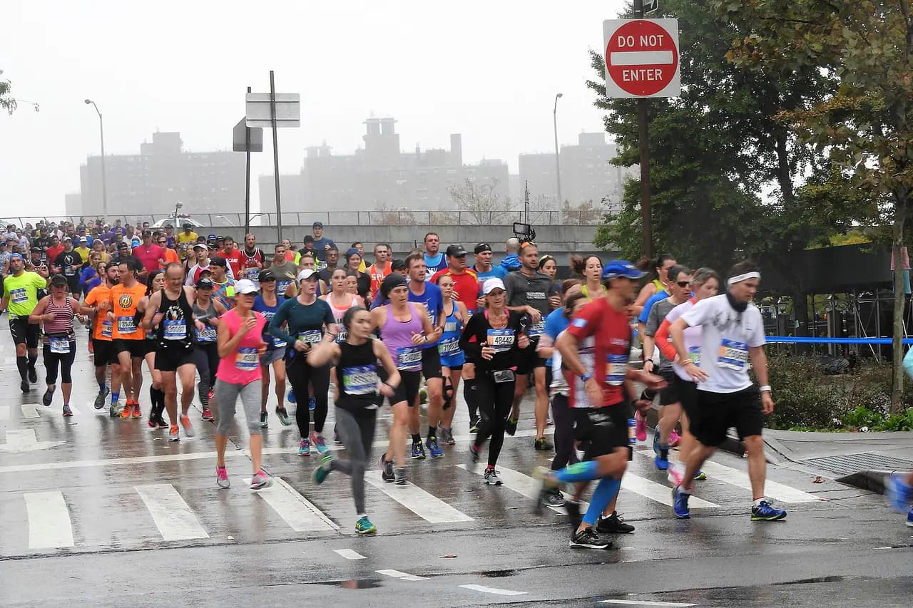 Marathon runners crossing East 138th Street in the Bronx under a gray sky