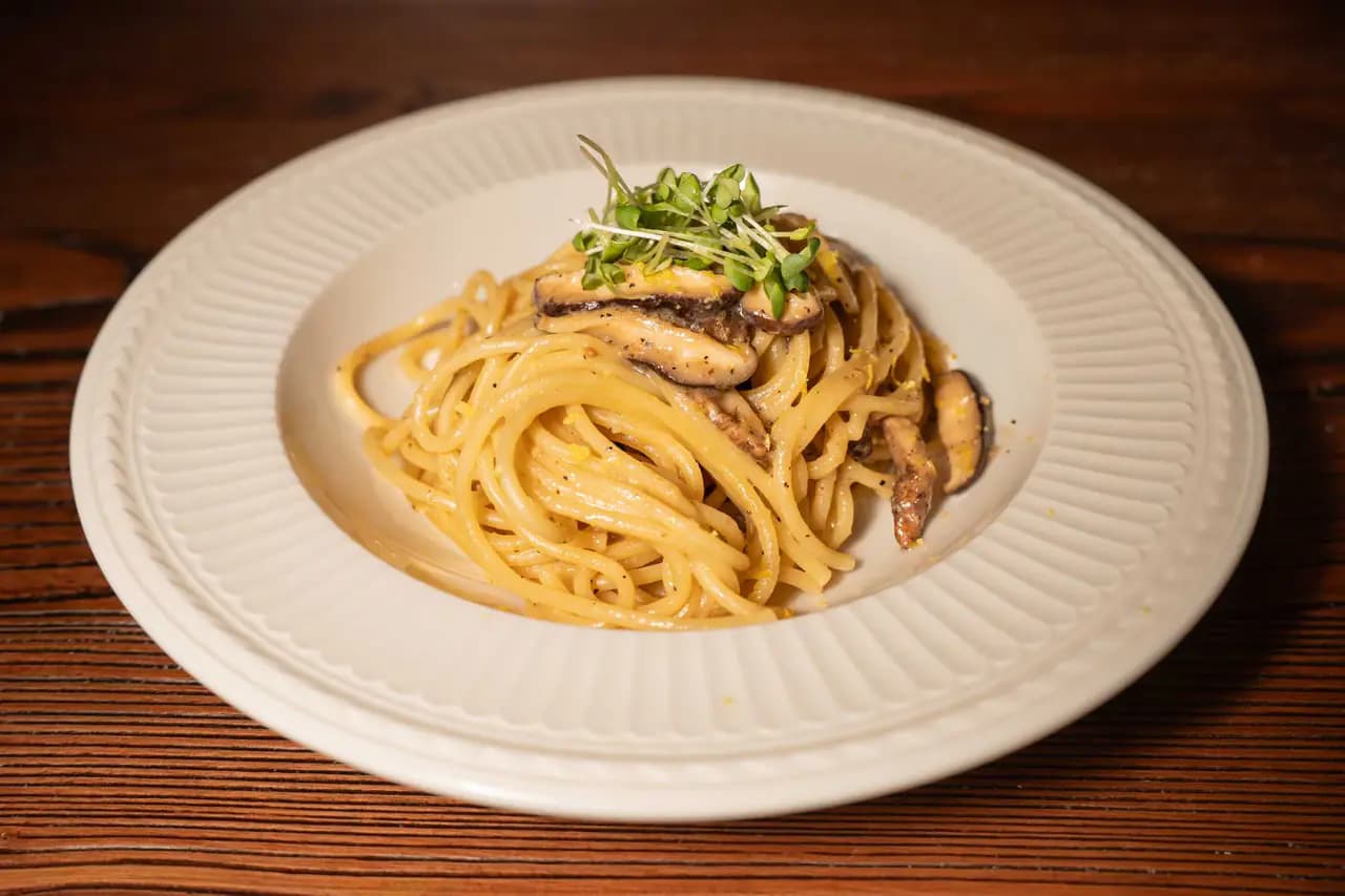A plate of doenjang shiitake pasta topped with sliced shiitake mushrooms and microgreens