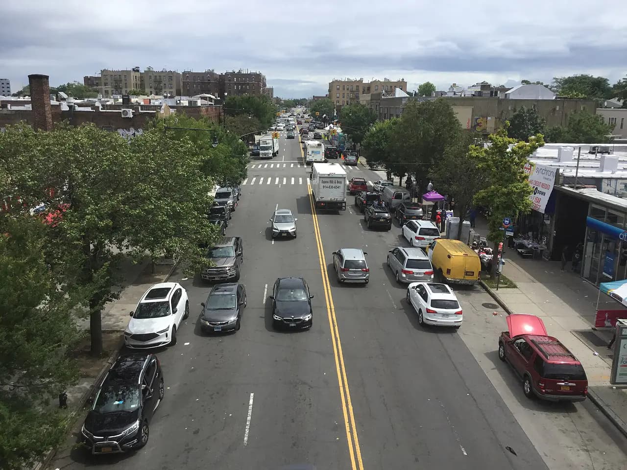 Allerton Avenue in the Bronx seen from the elevated subway station, with parked cars, shops and apartment buildings