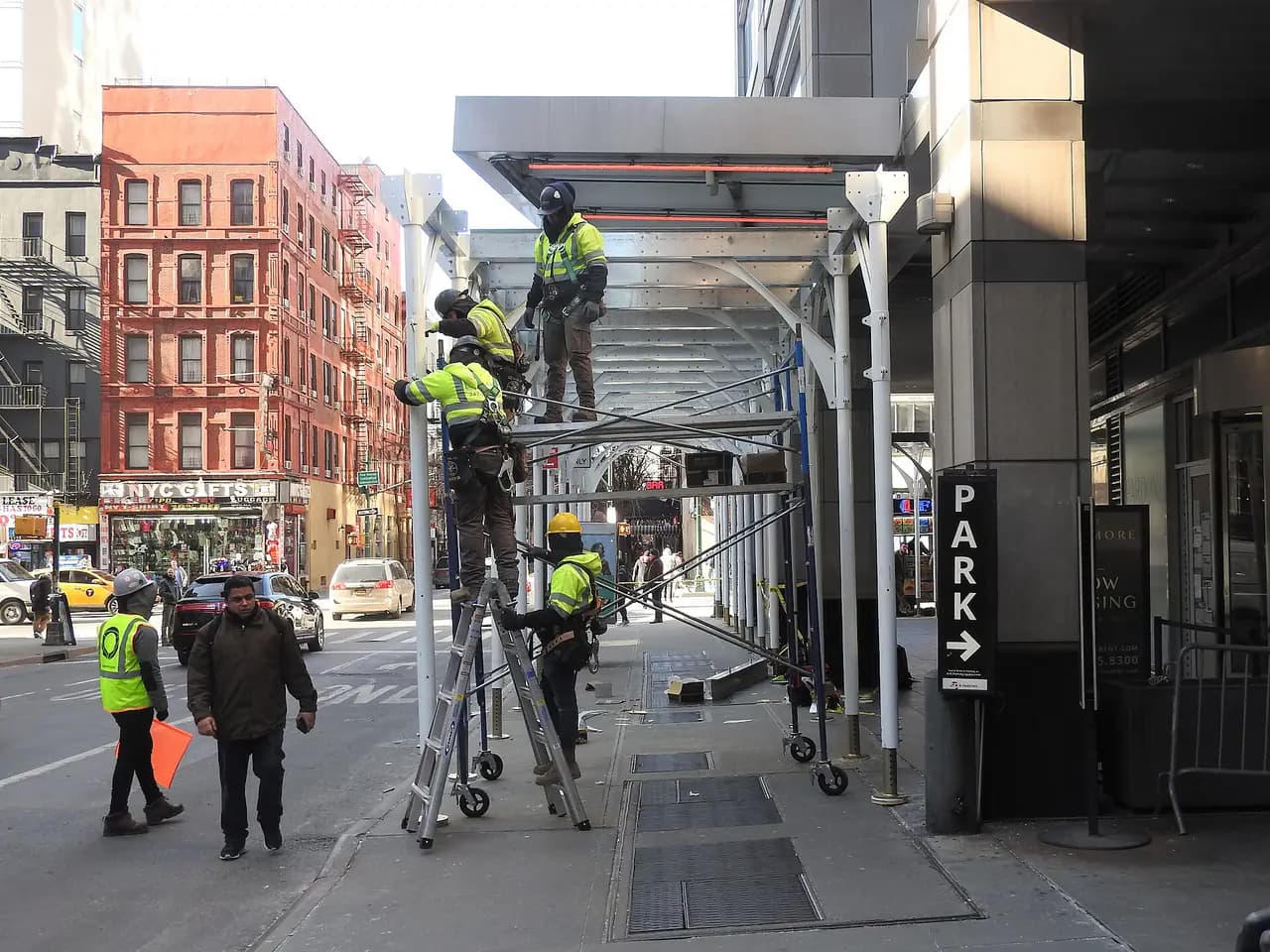 Workers in safety vests assembling a metal sidewalk shed on West 47th Street in Midtown Manhattan